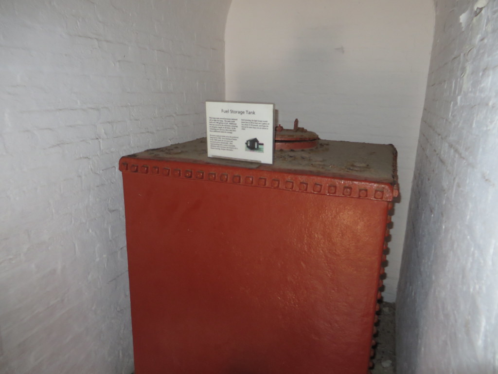 A large red fuel storage tank standing against a white-painted wall.